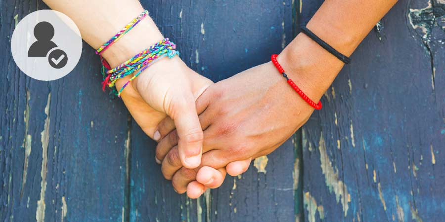 Two gay women wearing coloured wrist bands holding hands.